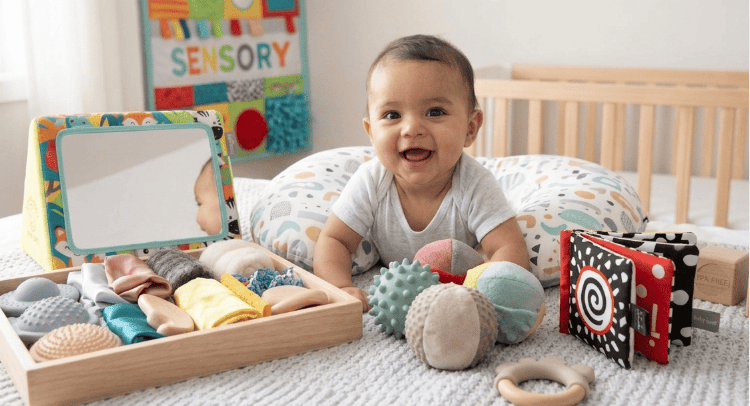 A 3-month-old baby lying on their tummy supported by a nursing pillow, surrounded by sensory balls, soft books, and a baby-safe mirror. Sensory Play for 3-Month-Olds